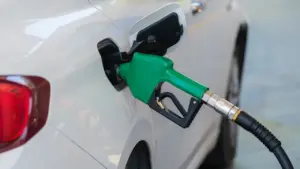 Baltas automobilis degalinėje pildomas degalais su žaliu degalų pylimo pistoletu