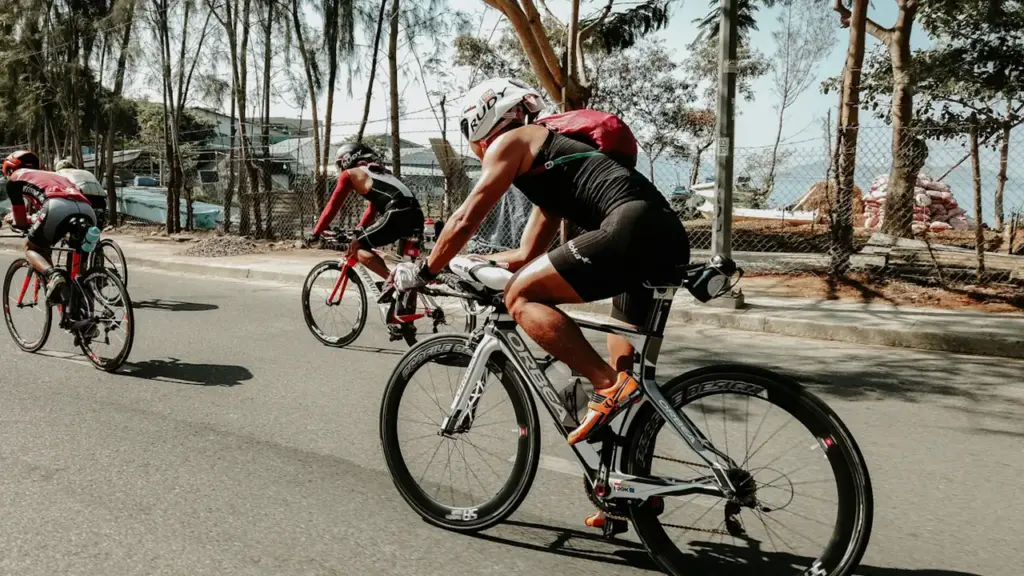 Triatloninkai važiuoja dviračiais plentu, ruošdamiesi artėjančioms sporto varžyboms Molėtų mieste.