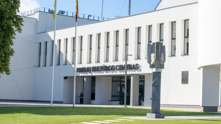 Modernus administracinis pastatas su Lietuvos vėliava, reprezentuojantis viešojo sektoriaus įstaigų veiklą ir paslaugas.