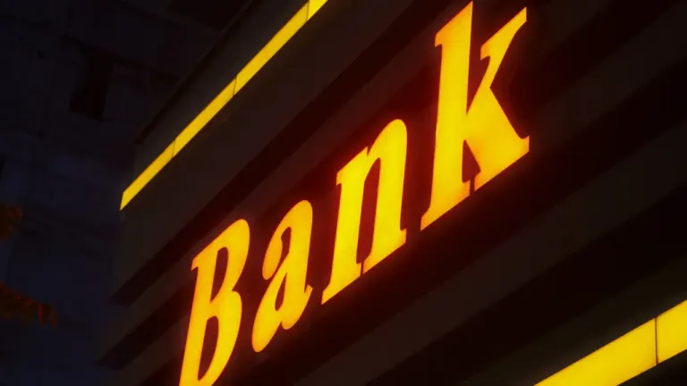 Šviečianti banko iškaba tamsiame fone, simbolizuojanti finansines operacijas ir bankines paslaugas Lietuvoje.