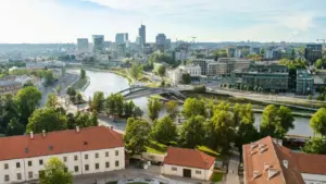 Panoraminis vaizdas į Vilniaus senamiestį su Neries upe, tiltu ir moderniais dangoraižiais fone.