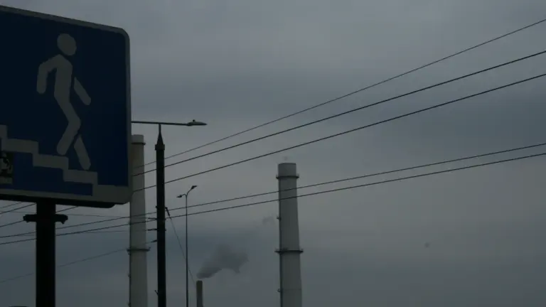 Vilniaus šilumos tinklų kaminai ir pėsčiųjų perėjos ženklas pilkame miesto fone.