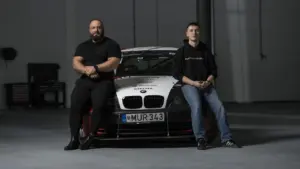 Du vyrai sėdi ant priekinio sportinio BMW automobilio gaubto tamsiame garaže.