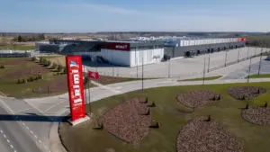 Didelis „Rimi“ logistikos centras su raudona stela ir Lietuvos vėliava saulėtą dieną.