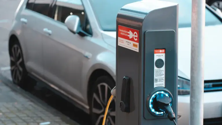 Elektromobilio įkrovimo stotelė gatvėje su prijungtu laidu ir stovinčiu automobiliu