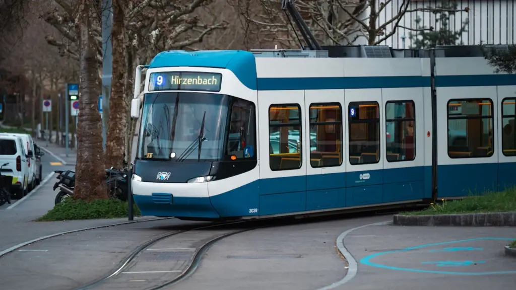 Mėlynas ir baltas tramvajus važiuoja bėgiais moderniame Europos miesto centre.