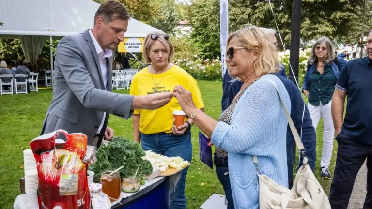 Vyras pilku švarku lauke bendrauja su žmonėmis prie stalo su maisto produktais.
